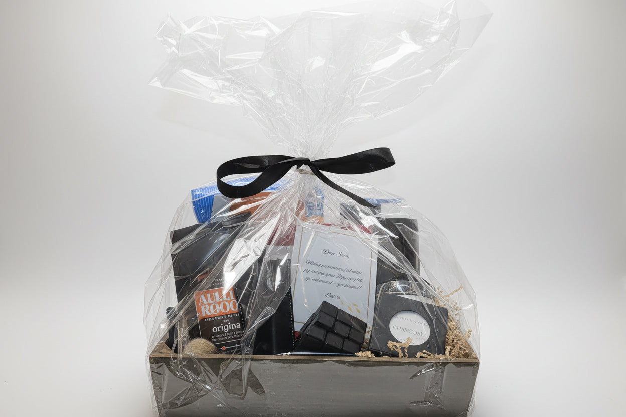 Gift basket with items wrapped in clear cellophane and a black ribbon on a white background