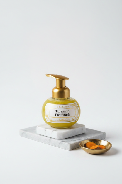 A bottle of Turmeric Face Wash with a white pump dispenser and yellow liquid, styled on a white marble block with turmeric roots, mint leaves, and dark amber bottles on a dark rustic wooden table.