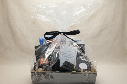 Gift basket with items wrapped in clear cellophane and a black ribbon on a beige background.